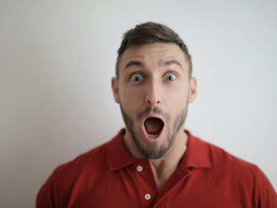 Portrait of a shocked man in a red polo shirt with a white background, expressing surprise.