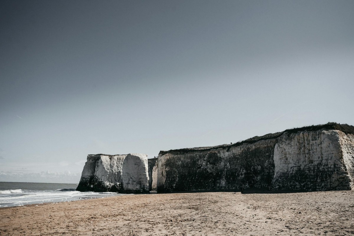 Majestic chalk cliffs overlooking a serene sandy beach on a clear day in Kent, England.