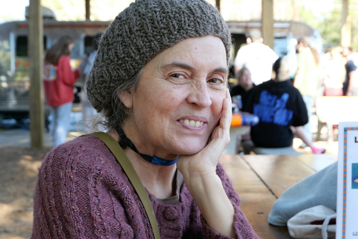 A woman in a knit hat smiles while sitting at an outdoor market in Gainesville, FL.