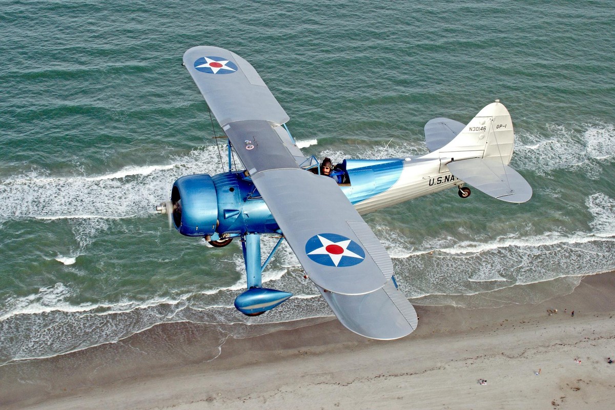 A vintage 1941 Waco biplane soars above Florida's beach, showcasing its iconic design and naval roundels.