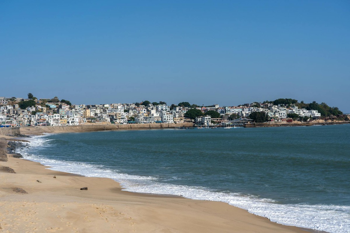 Picturesque view of a seaside town with a sandy beach and calm blue waters.
