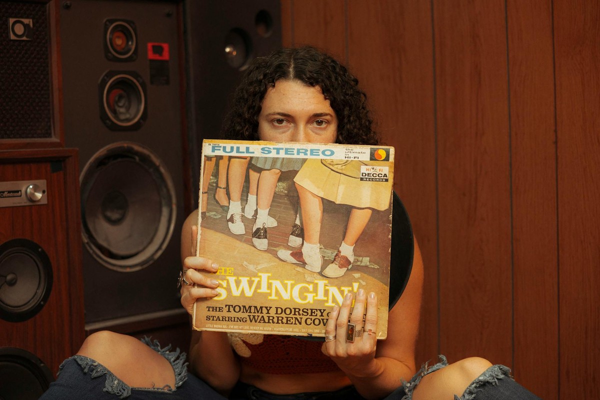 Person holding a vintage vinyl record in front of retro speakers, evoking a classic music ambiance.