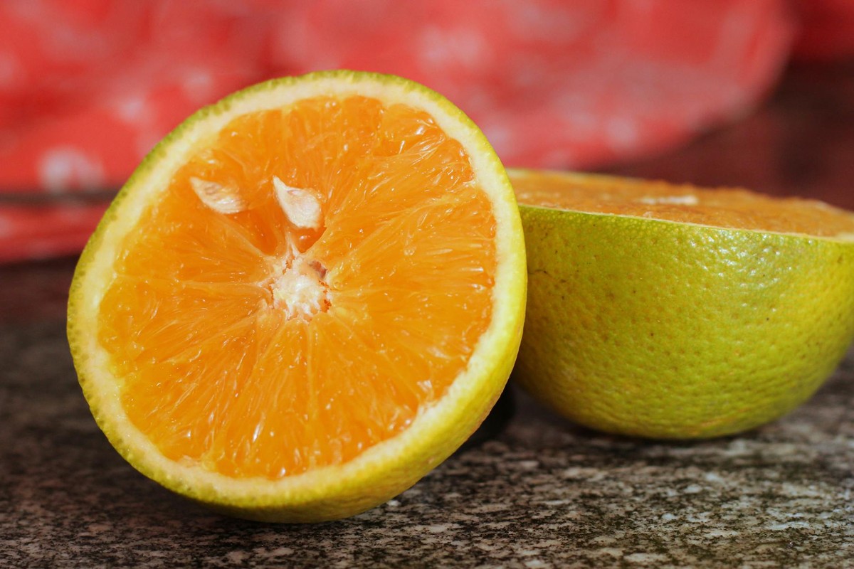 Vibrant close-up of a juicy orange sliced in half on a granite surface with a red cloth in the background.