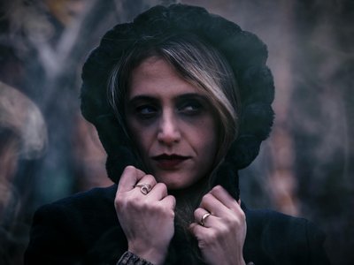 Close-up portrait of a woman in a black hood with a moody expression outdoors.