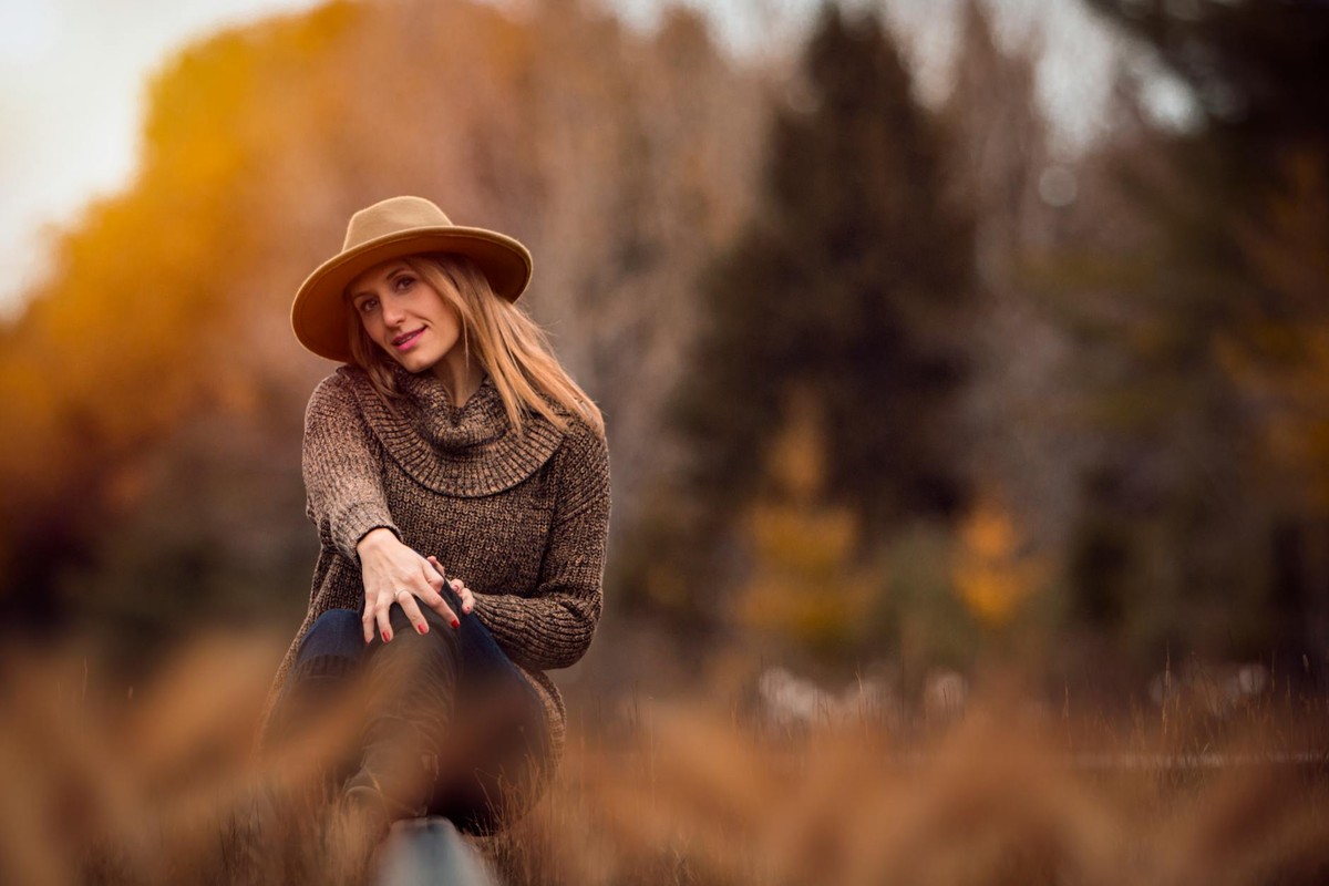 A vibrant autumn portrait of a smiling woman in a hat, enjoying the outdoors in a knitted sweater.