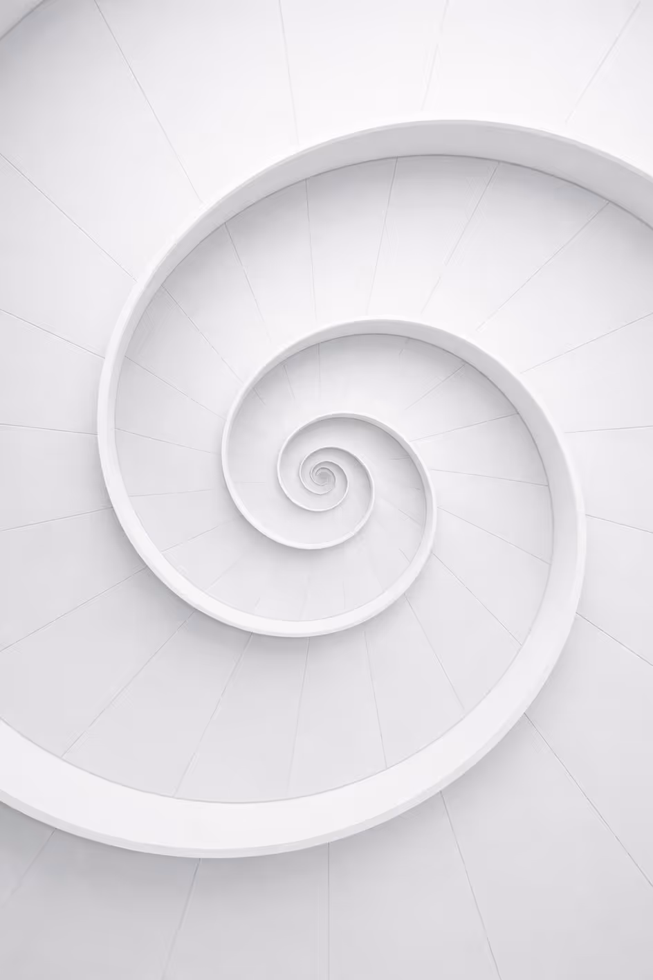 A high-angle shot of a white minimalist spiral staircase, symbolizing a structured engagement model, senior-led support, and alignment with portfolio growth.