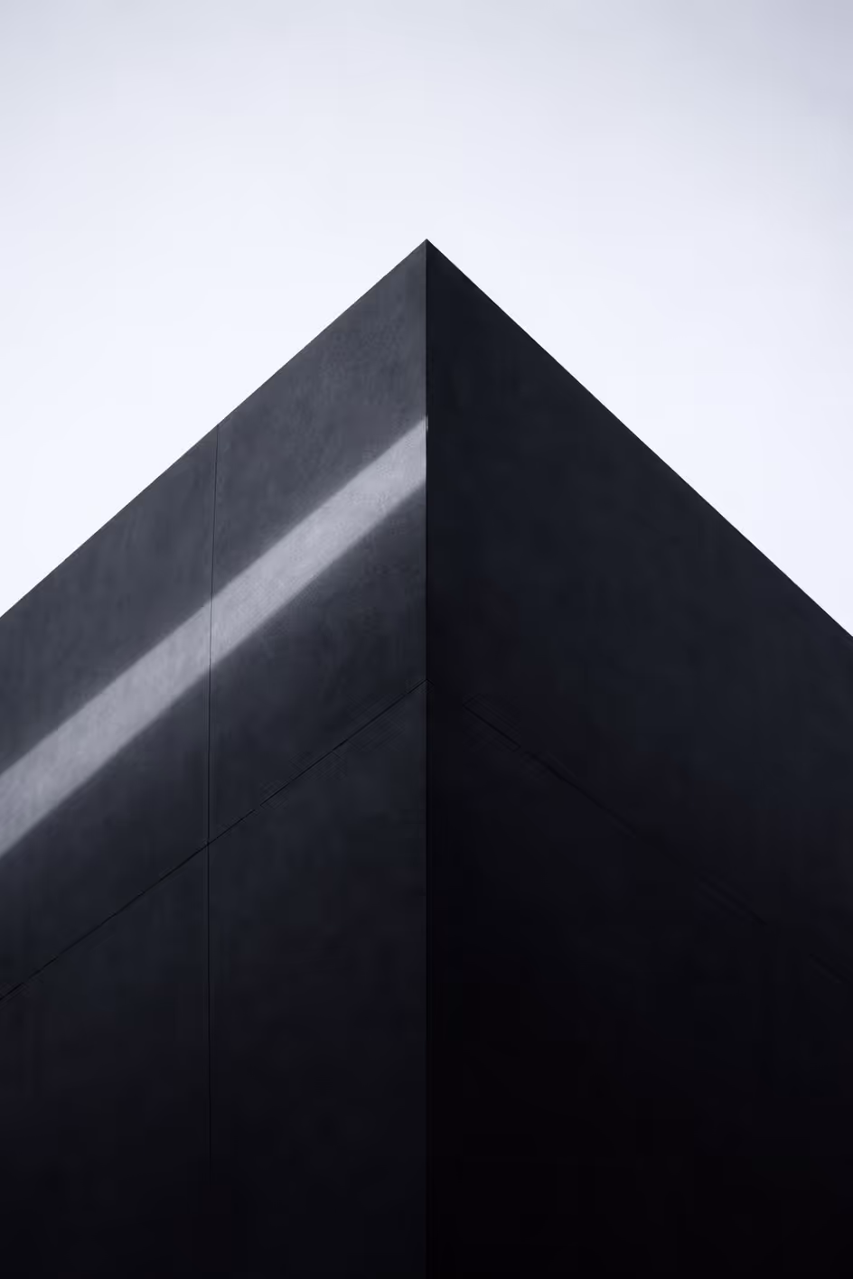 A minimalist shot of a dark geometric building corner with a sharp diagonal light beam, representing focused, independent, and senior-led operational insight.