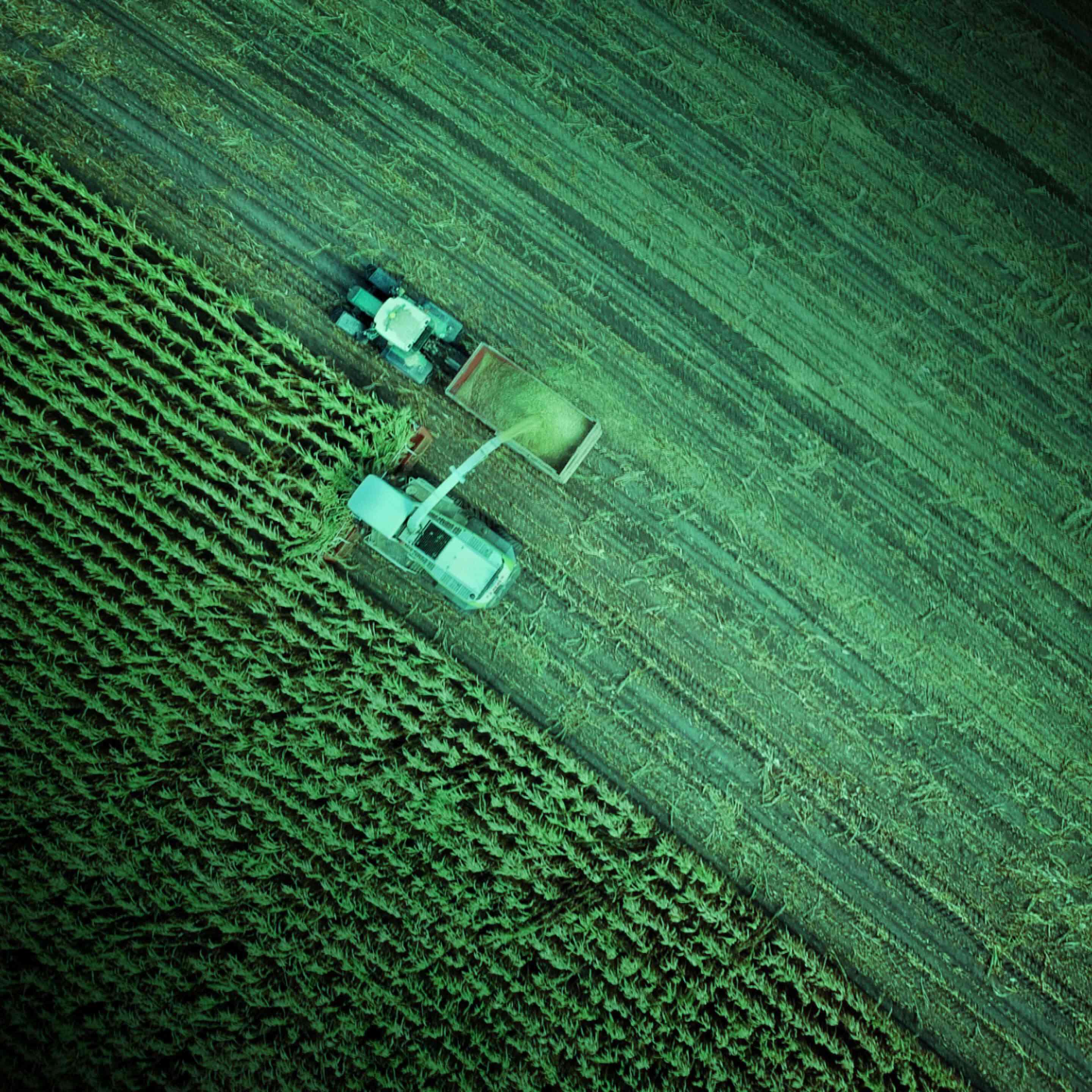 Aerial view of a harvester unloading harvested crops into a tractor trailer beside a cultivated field.