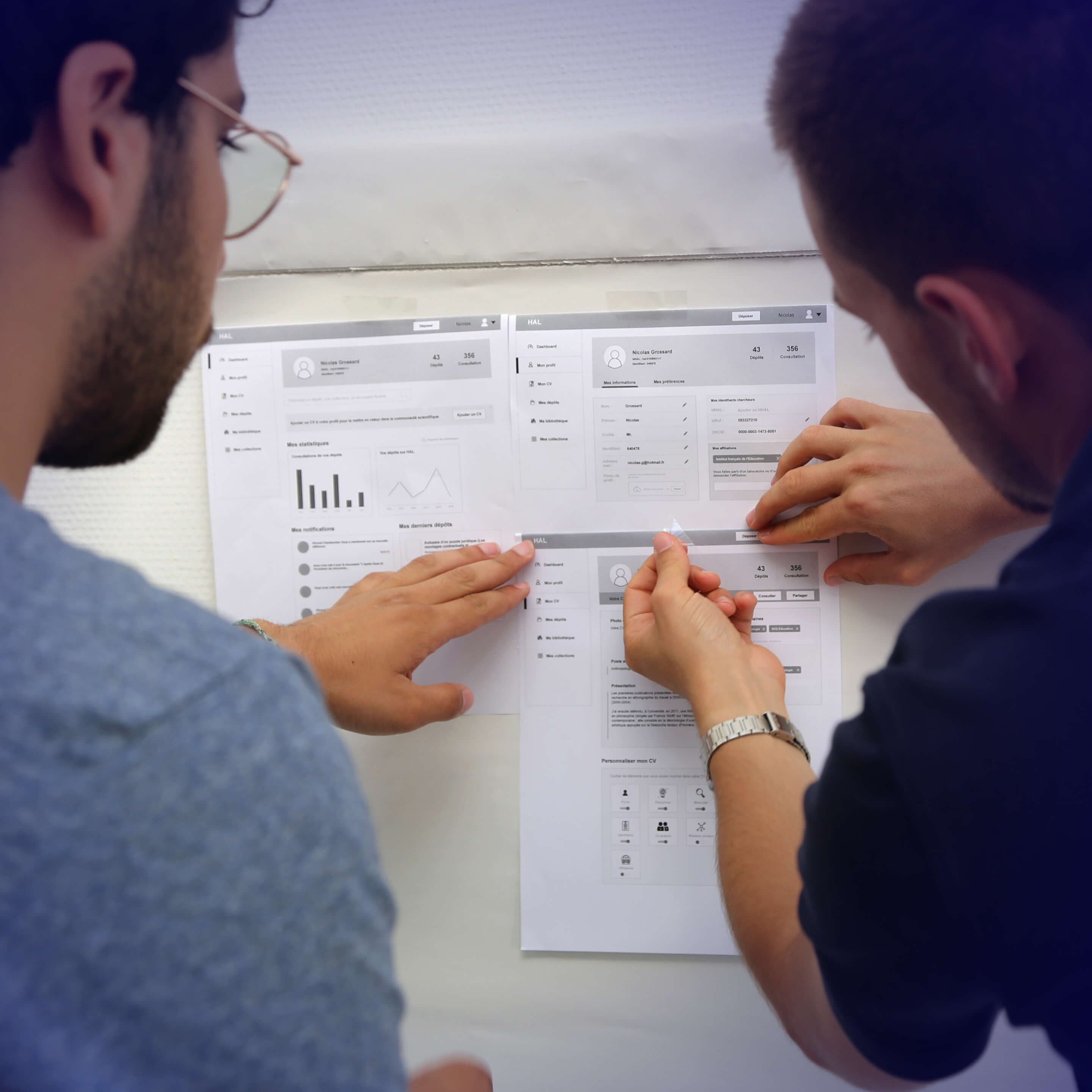 A colleague and me taping printed wireframe designs on a wall, working on app or website layout.