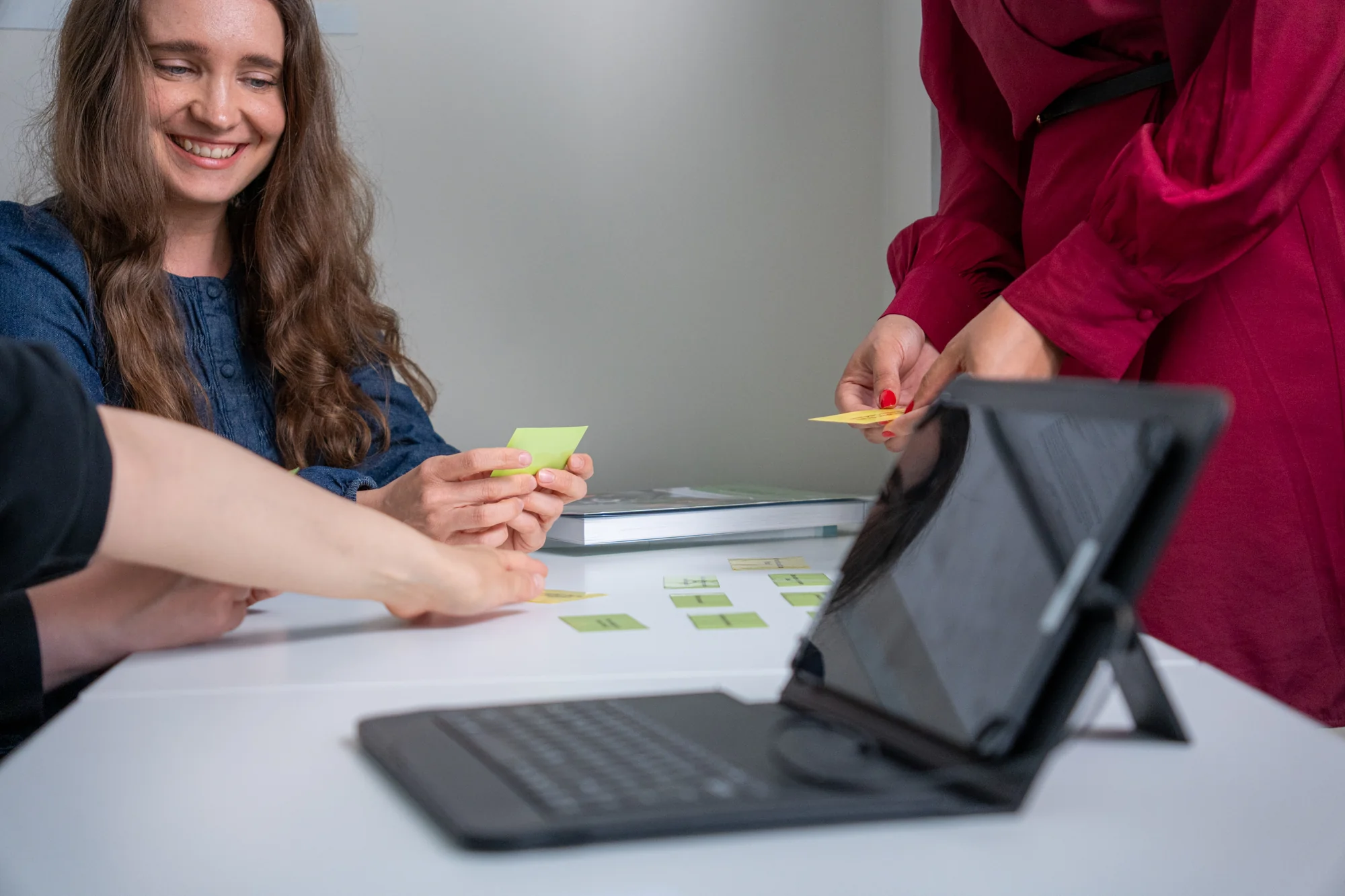 Personen arbeiten gemeinsam an einem Tisch mit Notizzetteln und einem Tablet mit Tastatur.