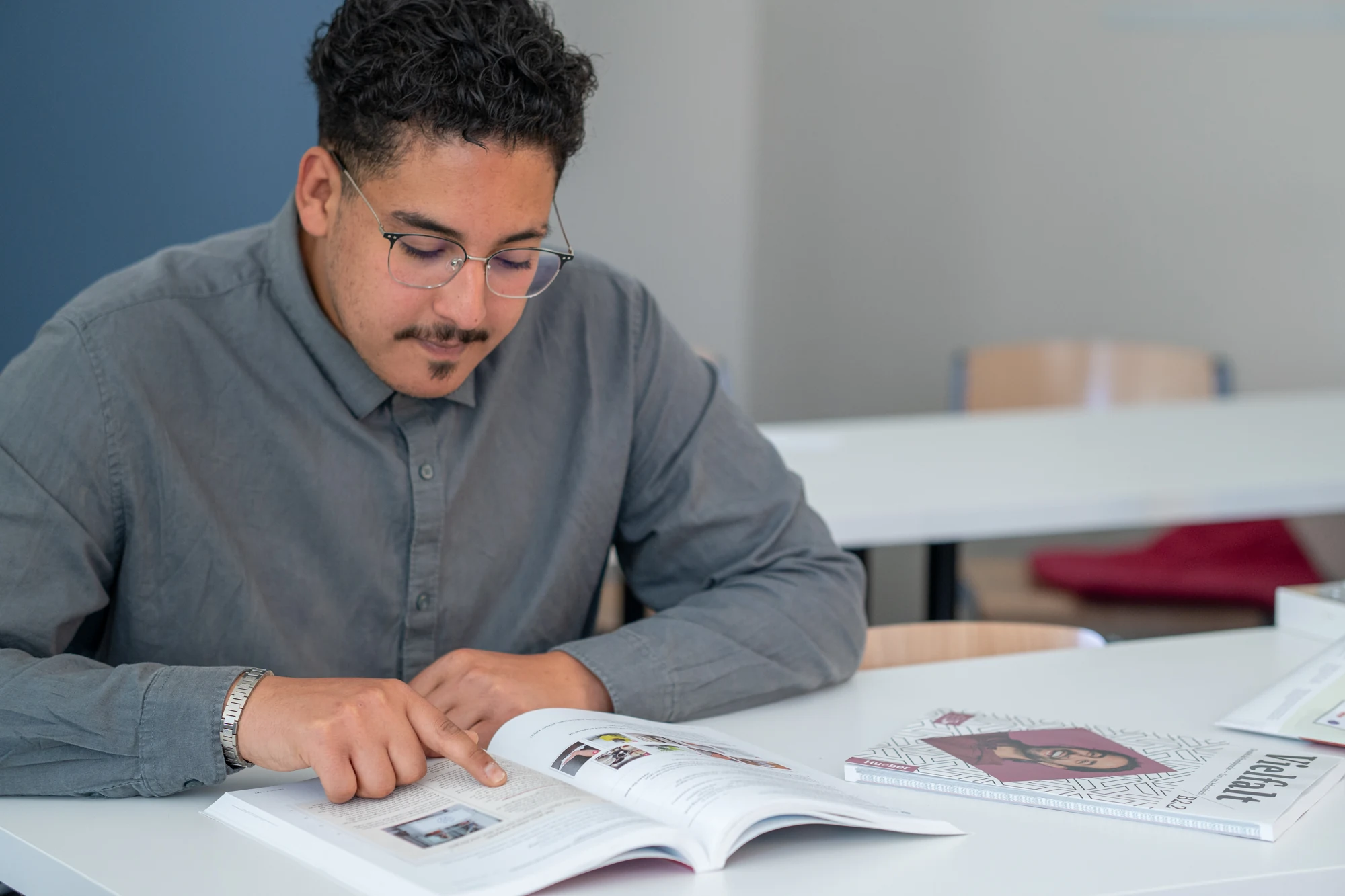 Mann sitzt an weißem Tisch und liest aufmerksam ein aufgeschlagenes Buch.