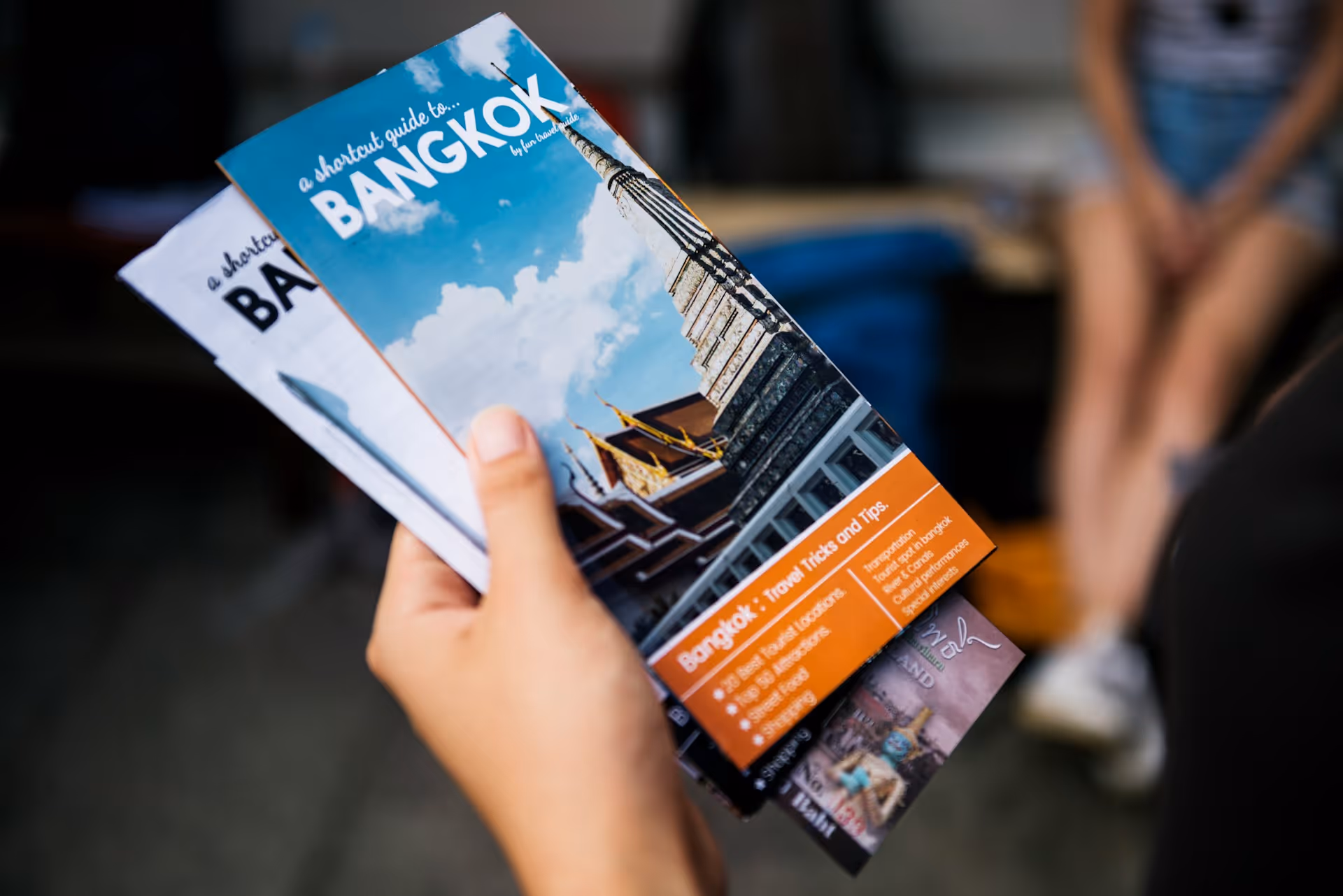 Nahaufnahme einer Hand, die detailliert gestaltete Bangkok-Reiseführer hält. Ein Beispiel für professionelles Grafikdesign, durchdachtes Layout und klare Typografie für hochwertige Printmedien und Markenidentität în Wien.
