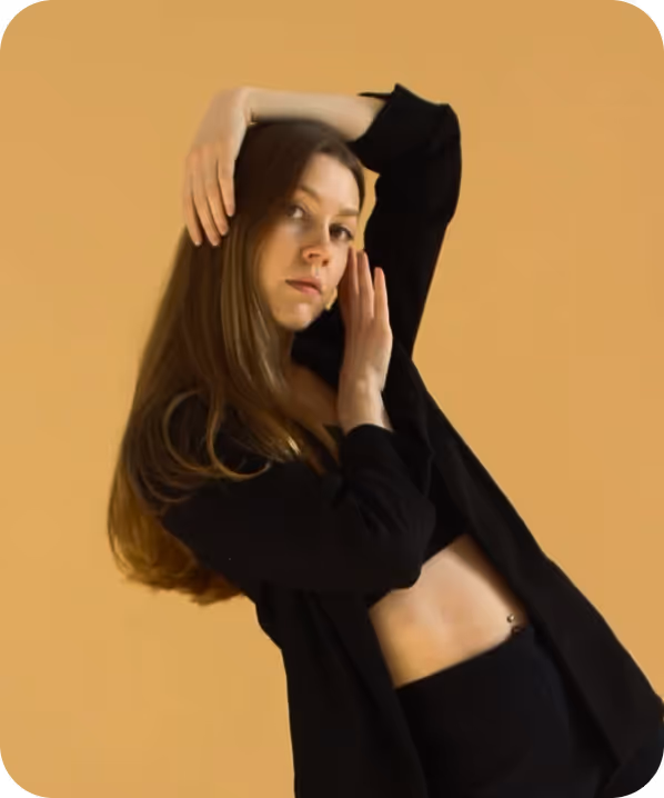 Woman with black curly hair wearing dark lipstick, a black bralette, and a sheer black shawl, showcasing a large chest tattoo and neck tattoo at a dimly lit indoor event.