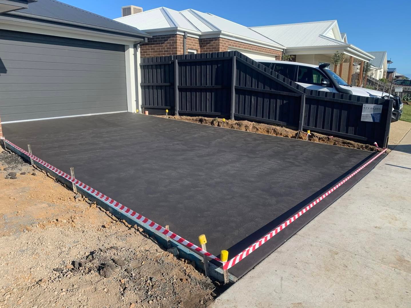 Freshly poured black concrete driveway in front of a modern house with a gray garage door and black wooden fence.