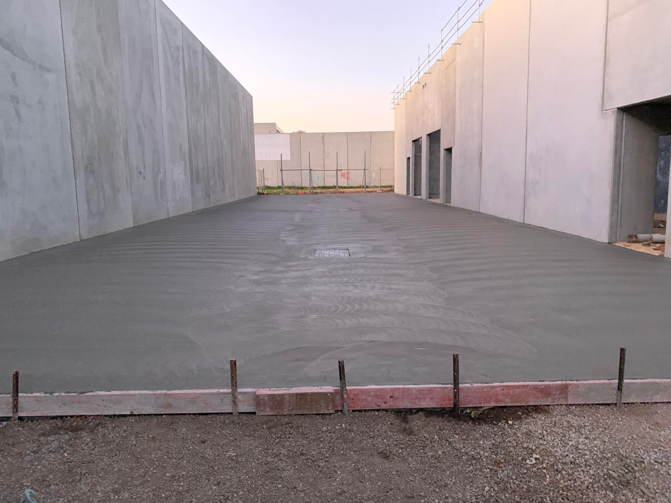 Freshly poured and smoothed concrete slab between two industrial building walls at dusk.