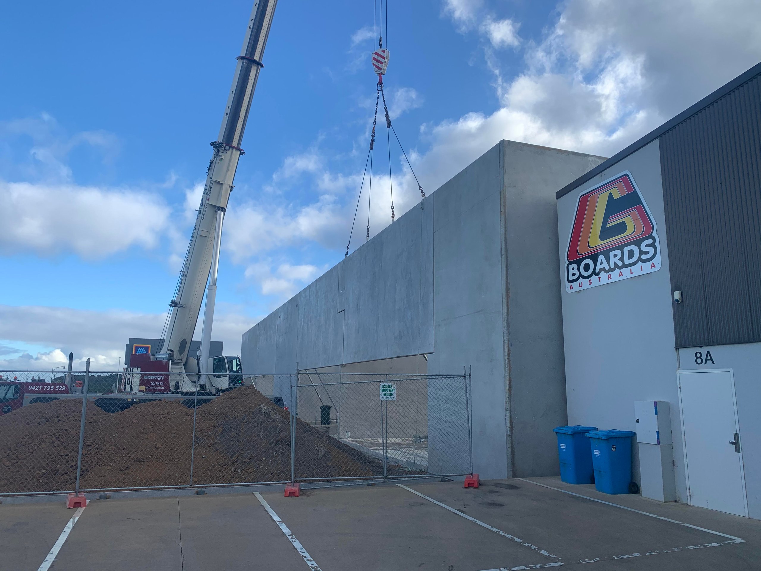 Crane lifting a large concrete wall panel at a construction site next to a building labeled G Boards Australia.