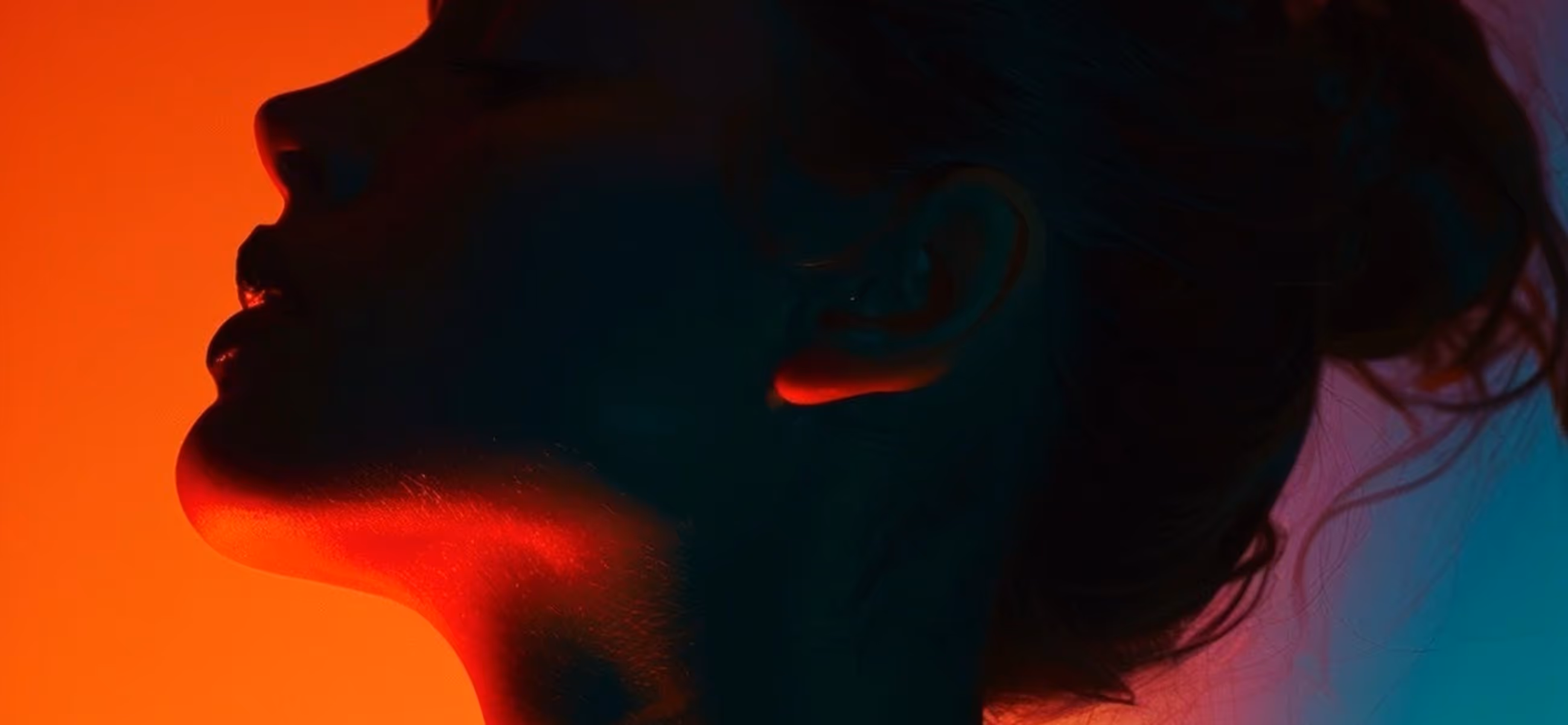 Profile of a woman’s face and neck illuminated by red and blue lighting against an orange and teal background.