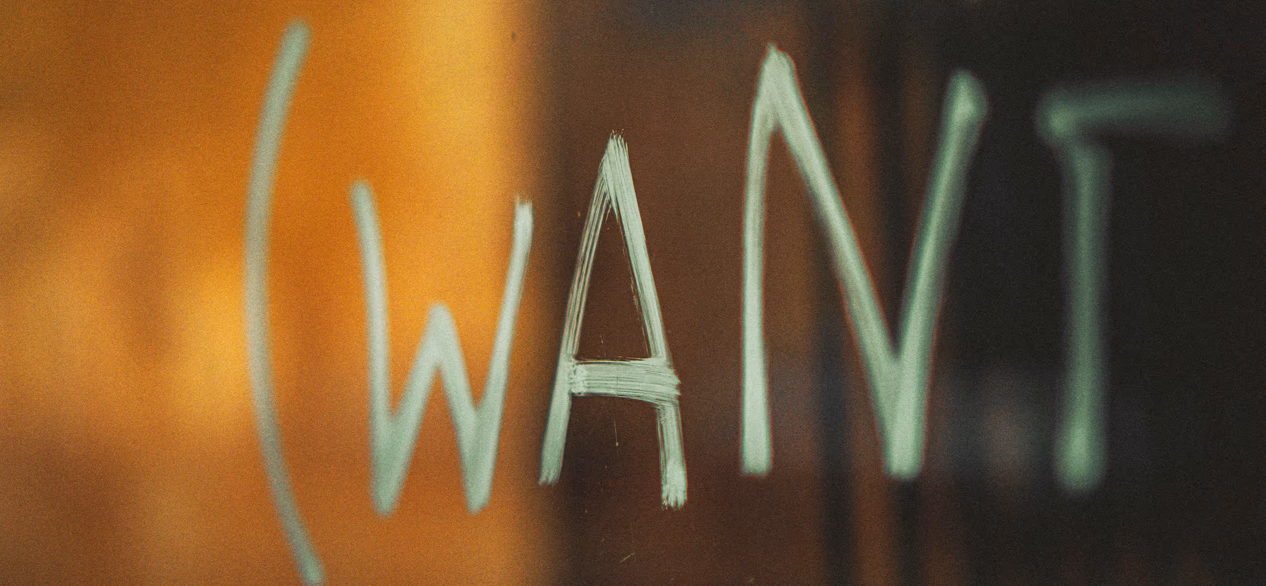 Close-up of the word 'GWAYT' written in white marker on a glass surface with a warm background.