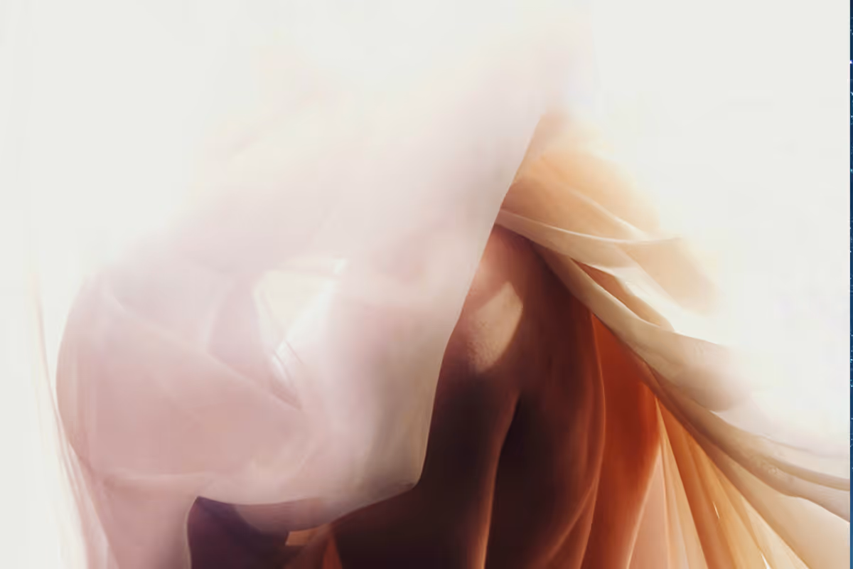 Softly lit artistic image of a partially obscured nude figure wrapped in translucent fabric.