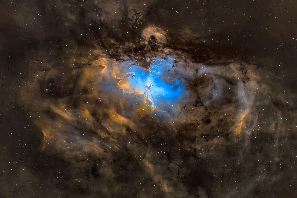 Nebula in space with blue, orange, and dark dust clouds and numerous scattered stars.