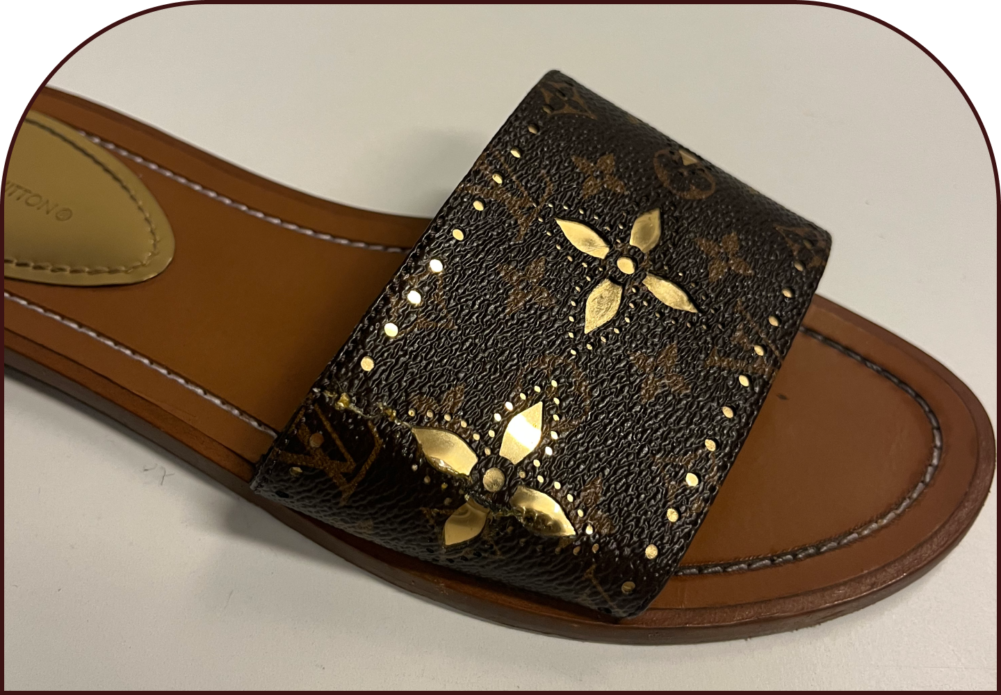 Close-up of a Louis Vuitton monogram canvas slide sandal with gold studded floral embellishment.