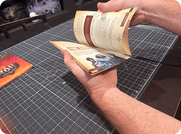 Hands flipping through a printed tabletop game rulebook.