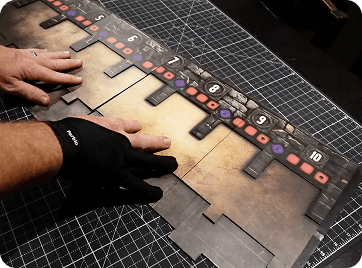 Hands assembling a large physical Battle Ark game board on a cutting mat.