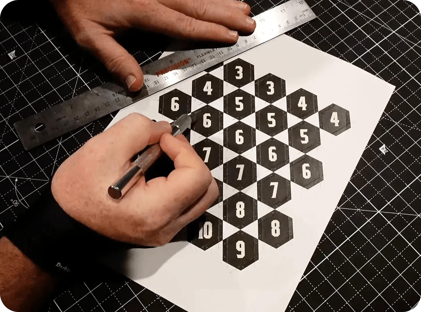 Hands cutting and preparing numbered tiles on a cutting mat during physical prototype production.