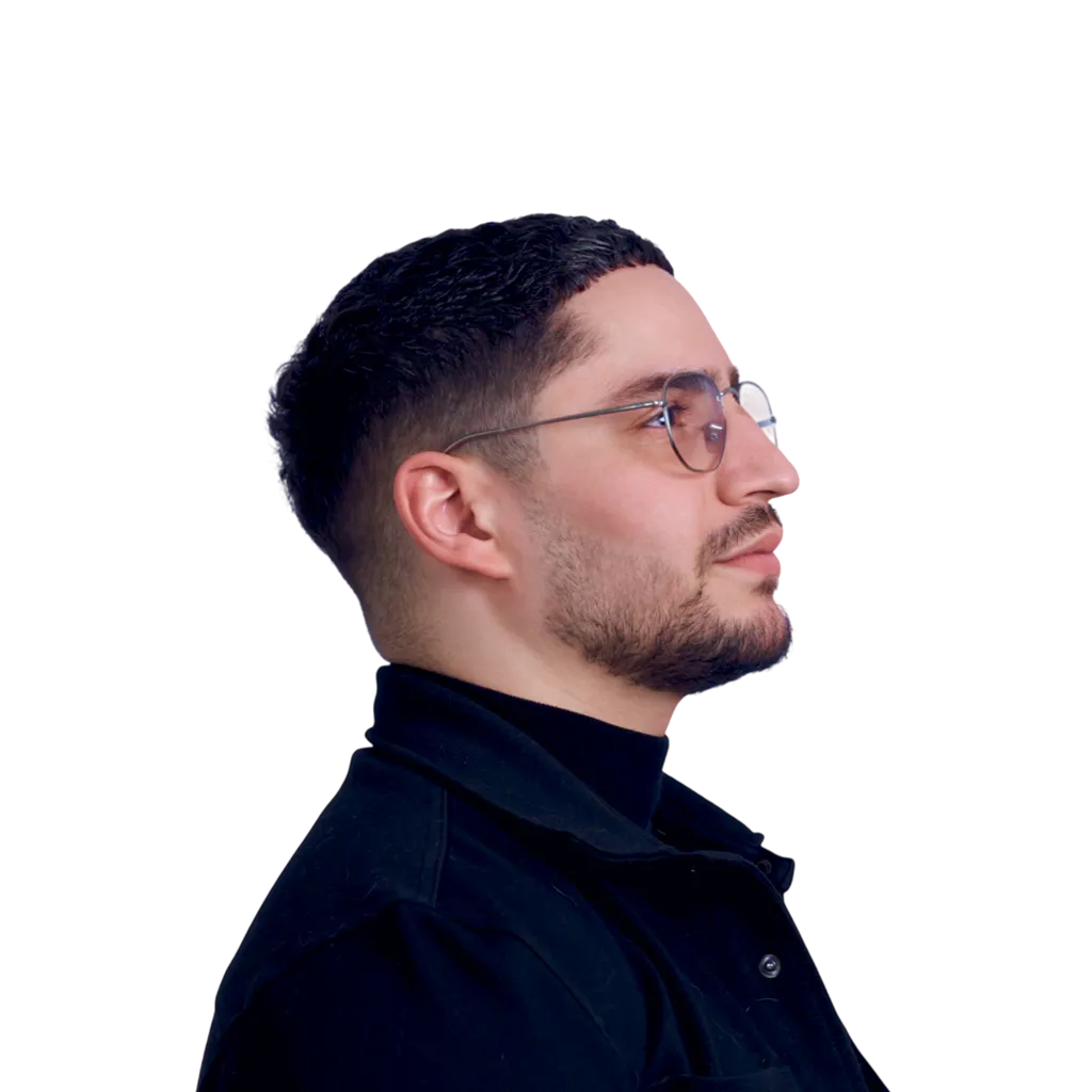 Portrait en noir et blanc d'un homme portant des lunettes, avec une barbe courte et coiffure courte, vu de profil vers la droite.