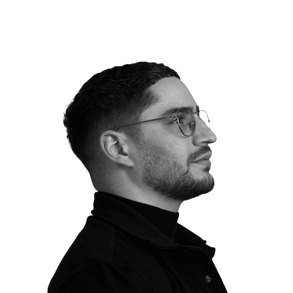 Portrait en noir et blanc d'un homme portant des lunettes, avec une barbe courte et coiffure courte, vu de profil vers la droite.