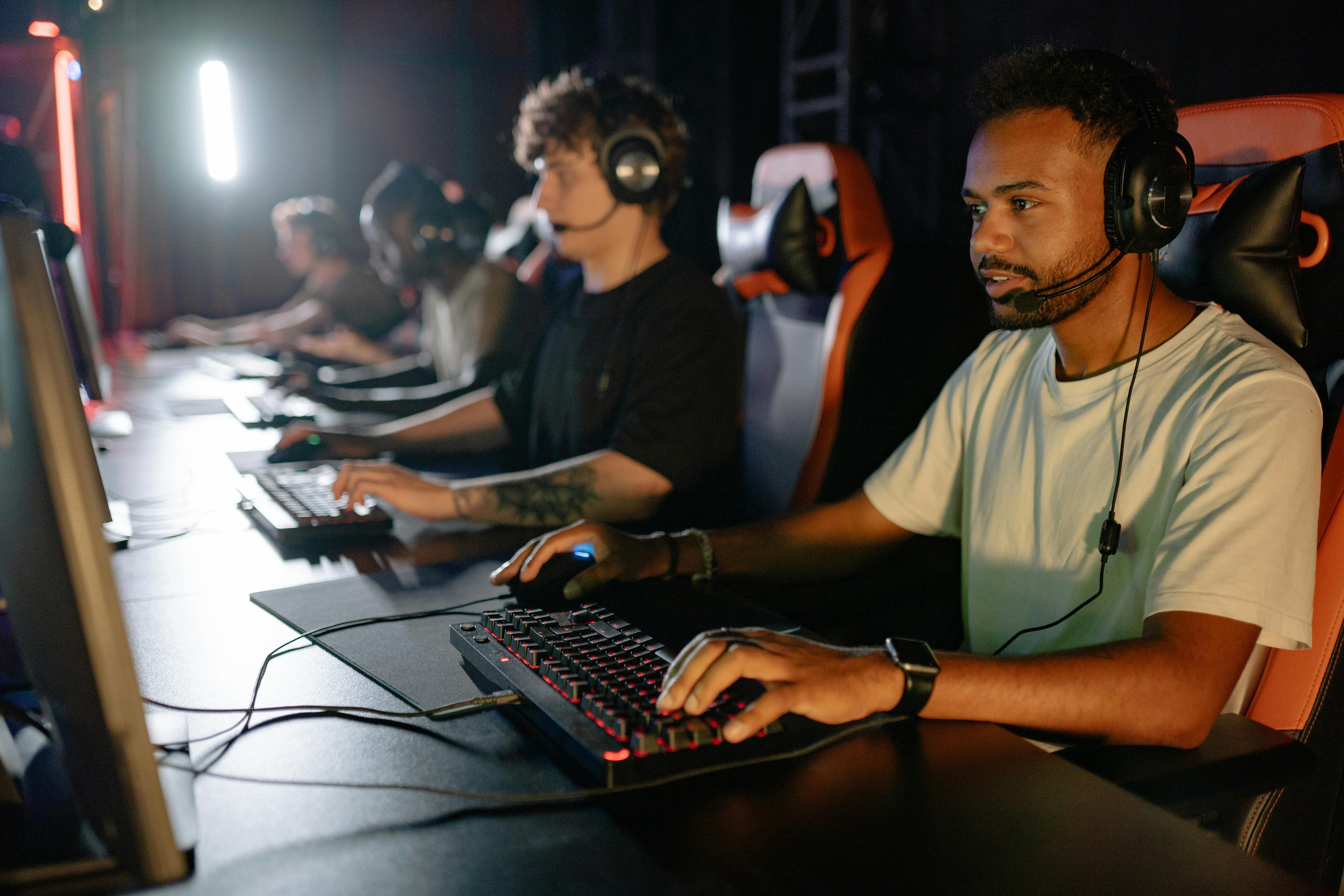 Group of young gamers wearing headsets playing on computers in a dimly lit gaming setup.