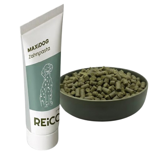Tube of MAXiDOG Zahnpasta toothpaste next to a bowl filled with small cylindrical green pellets.