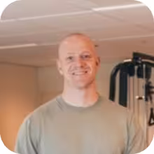 Smiling bald man wearing a gray shirt in a gym setting.