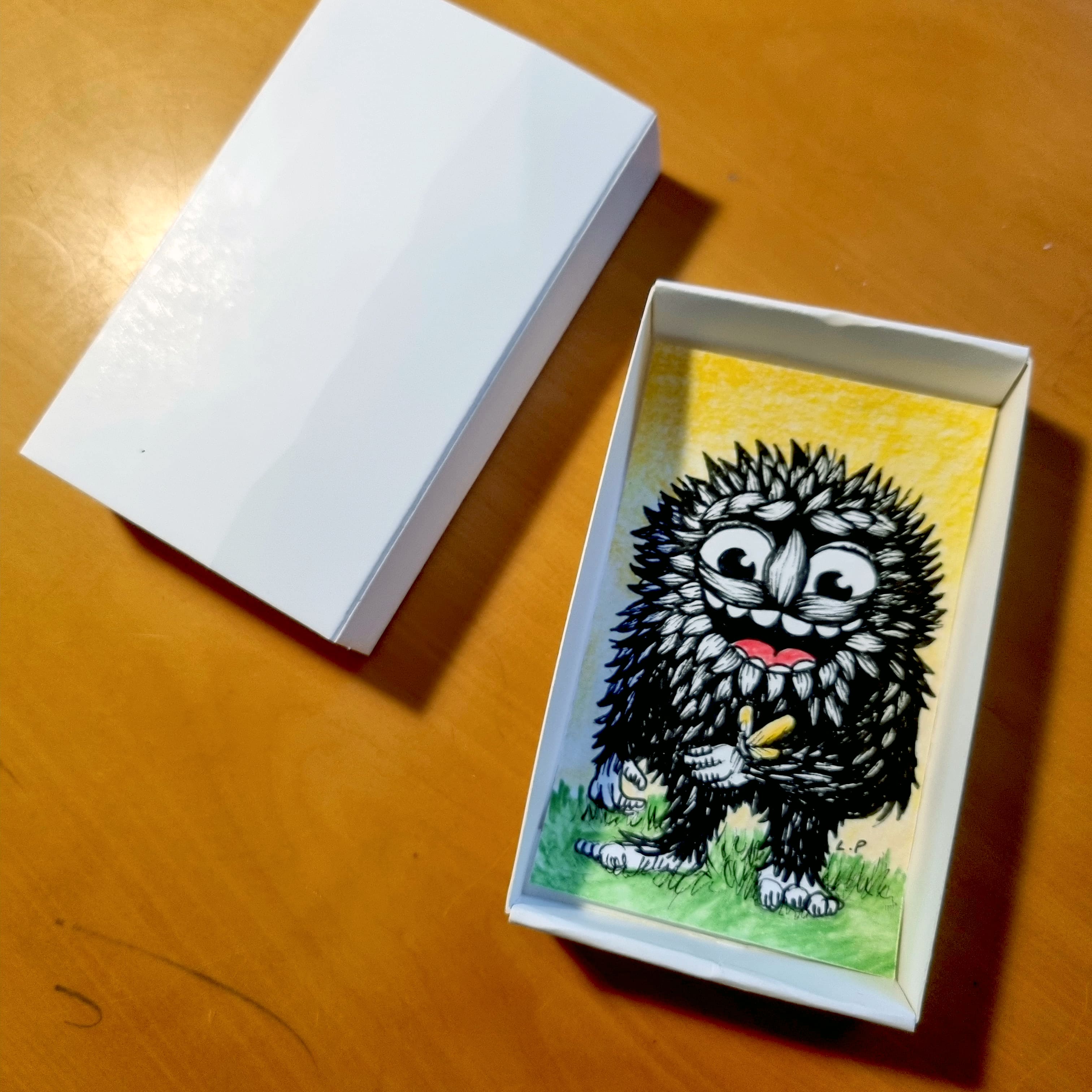 Cute drawing of a black monster in a white paper box.