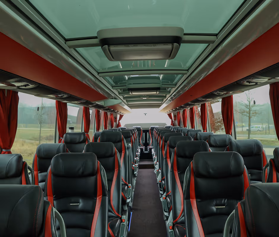 Interieur van een luxe autocar met zwarte leren stoelen en rode accenten, grote ramen en een glazen dak.