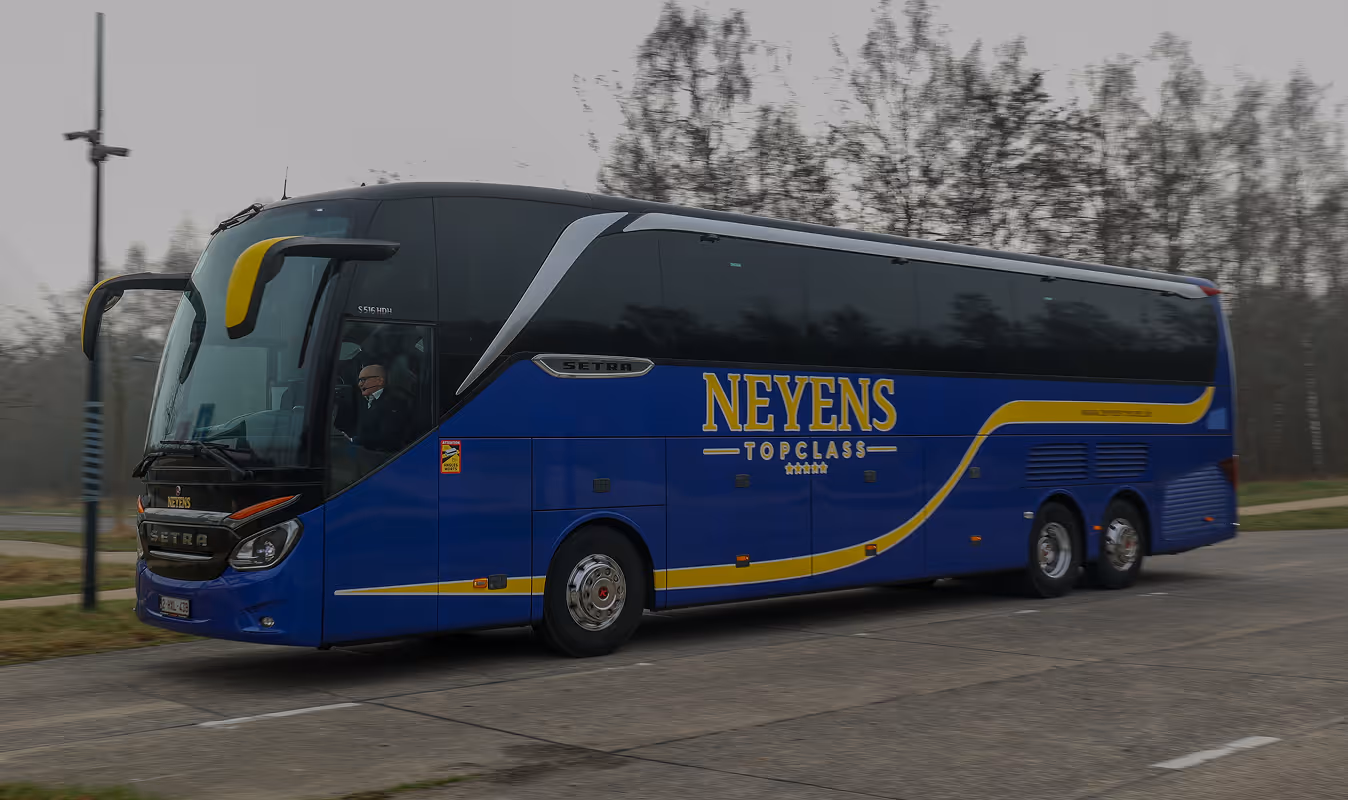 Blauwe touringcar van Neyens Topclass met gele accenten, rijdend op een weg met bomen op de achtergrond.