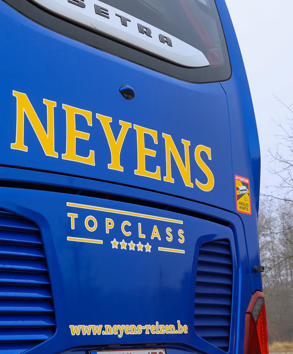 Close up van de autocar bus waar op staat "Topclass Neyens" waarmee vakanties en groepsreizen worden georganiseerd.