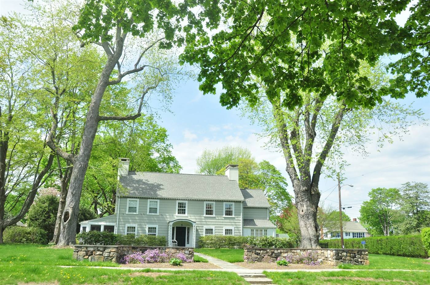 Classic New England home with a stone wall, mature shade trees, and a green lawn
