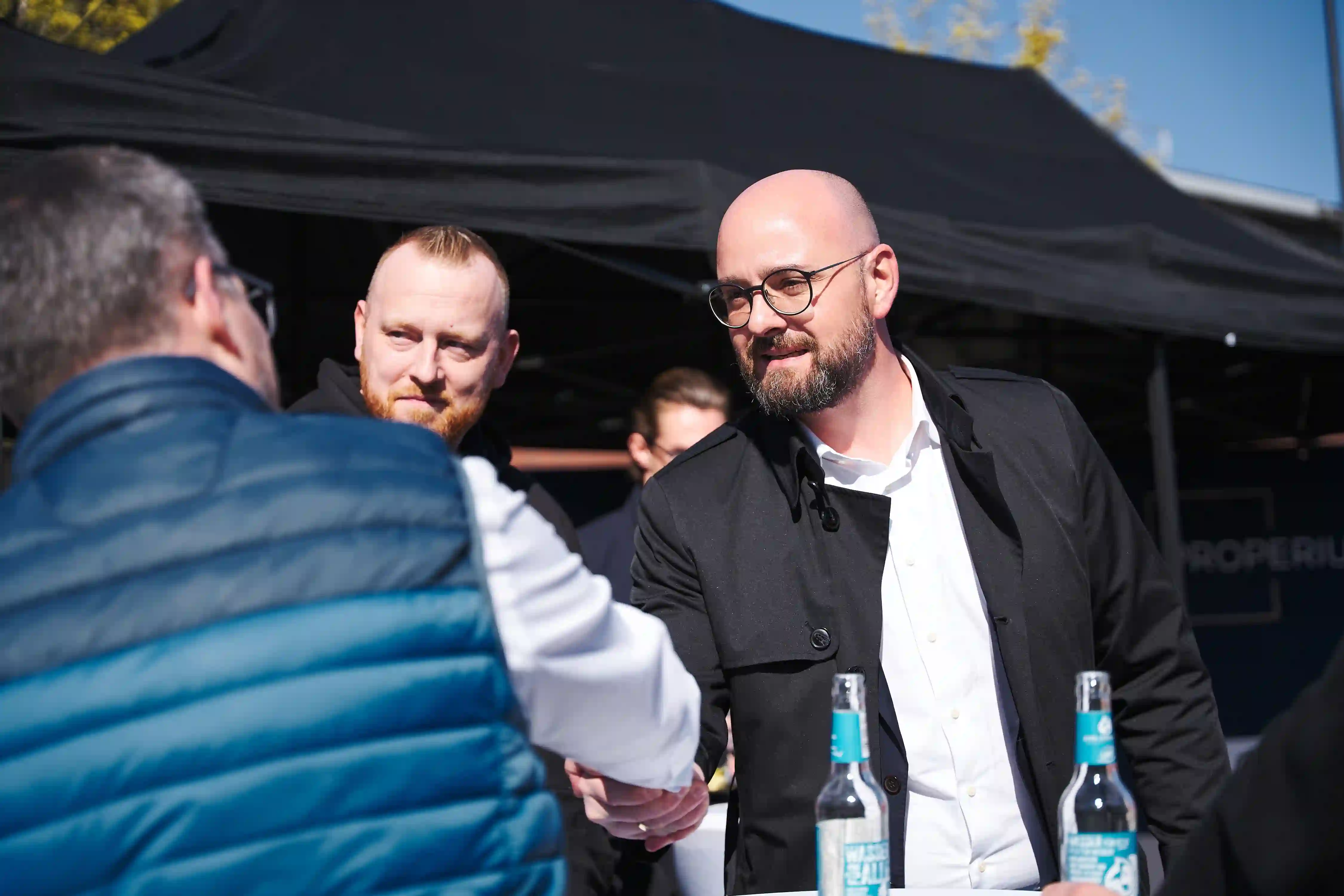 Zwei Männer schütteln sich die Hand vor einem schwarzen Pavillon