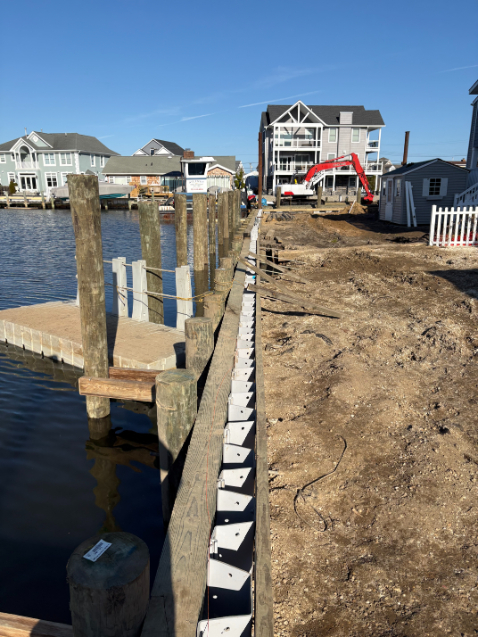 Link-Belt excavator operating from a marine barge installing timber dock pilings for waterfront construction project.