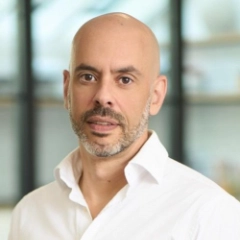 Portrait of a bald man with a trimmed beard wearing a white shirt, with a blurred background.