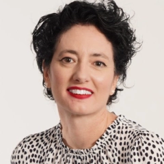 Smiling woman with short curly black hair wearing a white blouse with black spots.