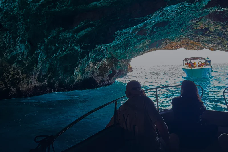 Entering the Blue Cave by boat, turquoise water with passengers silhouetted while another boat passes through the cave opening.