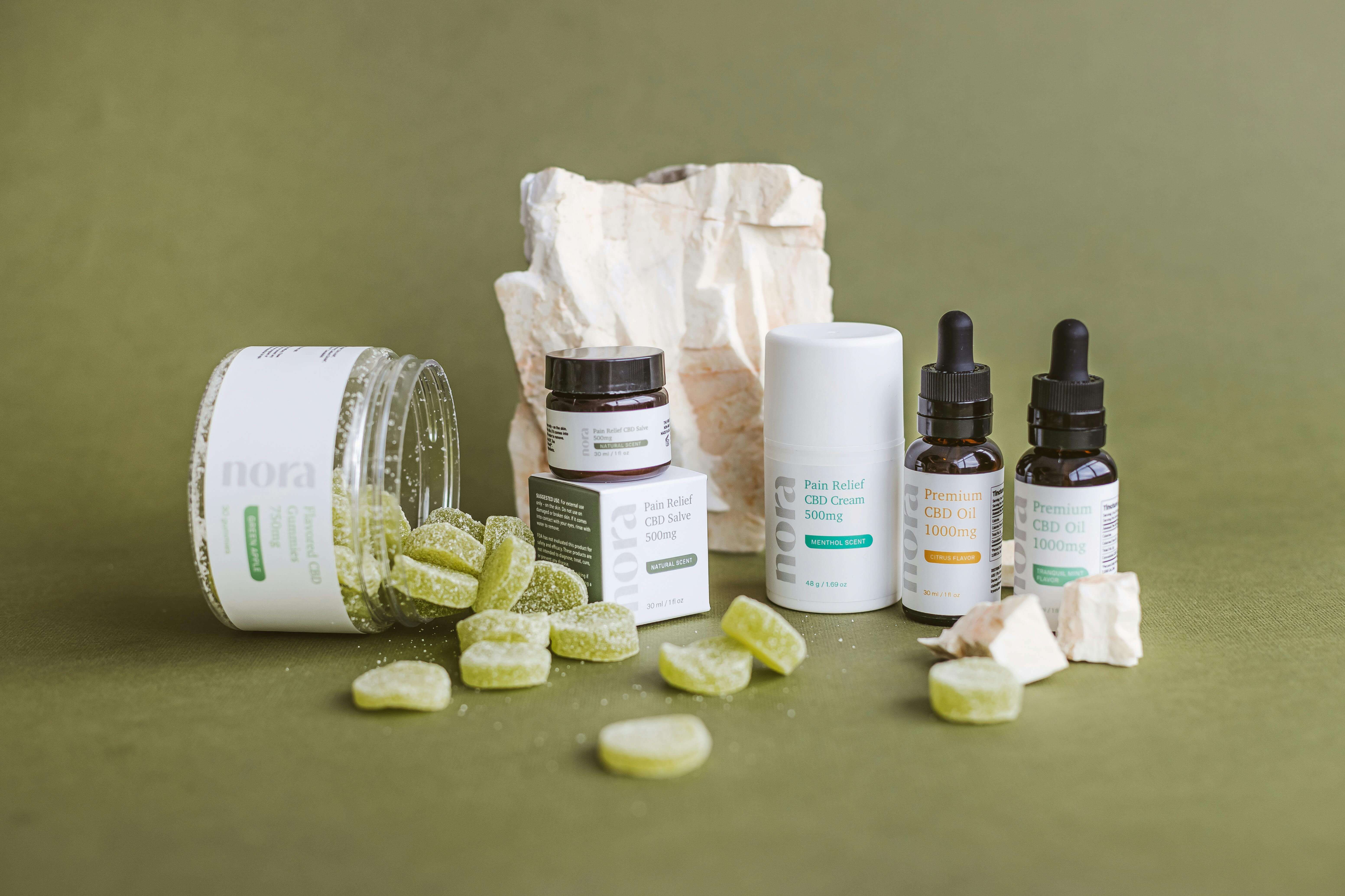 A light green table scape with gummy supplements spilled on table on the left side, jar tipped over. The middle and right side showcases cosmetics packaging for creams in jars and boxes and glass tinctures.