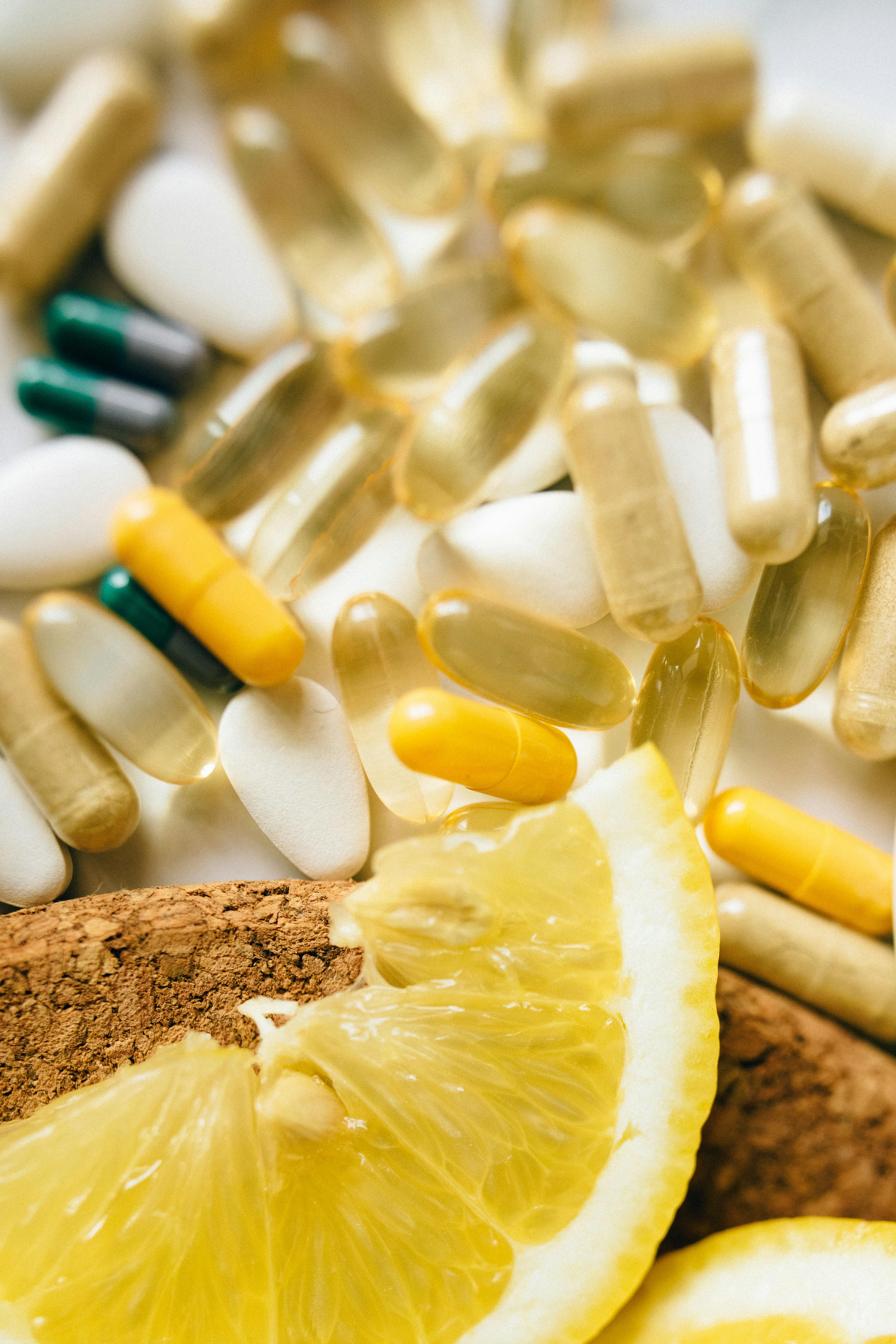 Lifestyle photograph with an array of supplements that are gelatin caps or sealed capsules that are all organic or yellow. Lemon slices and cinnamon are in the foreground.