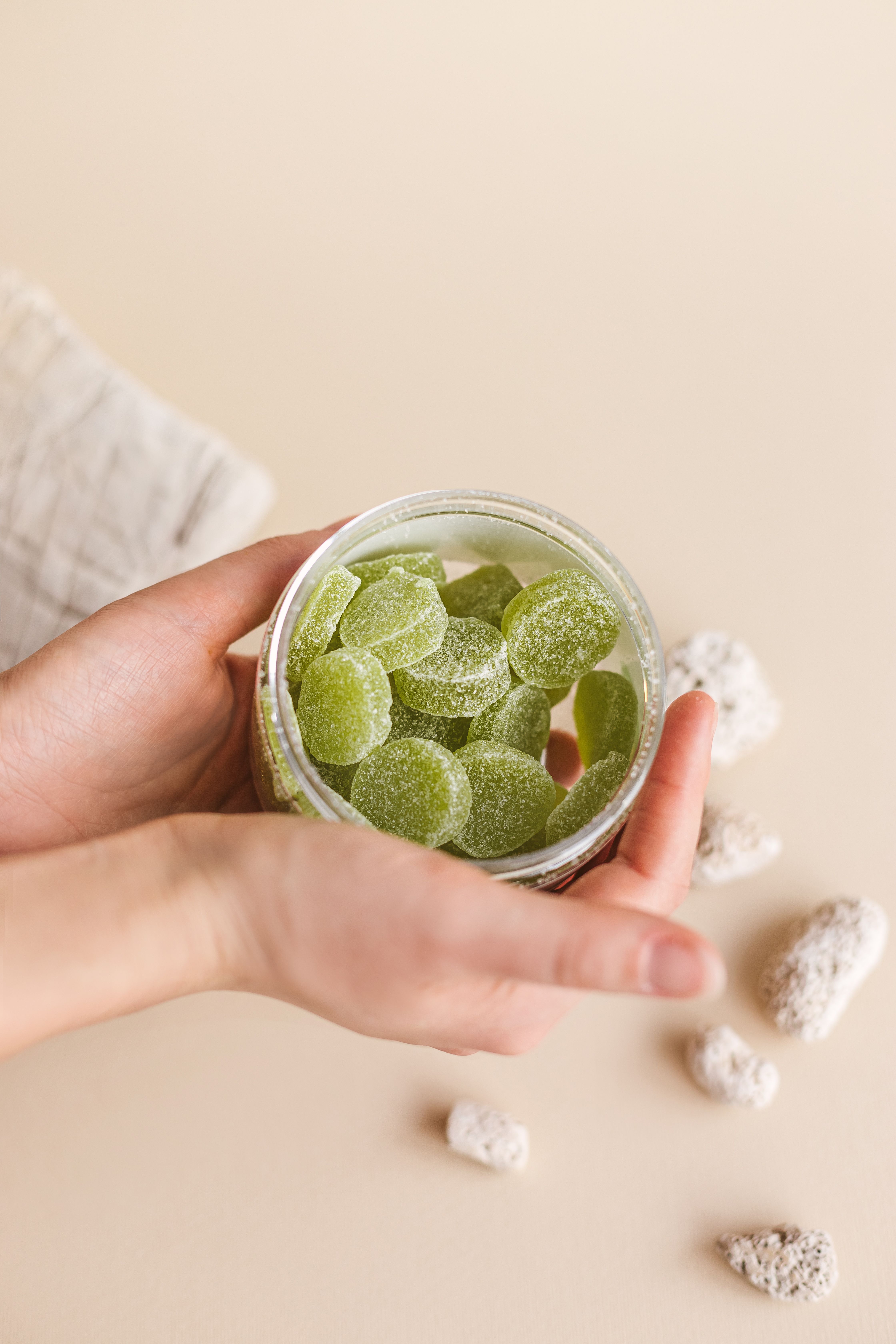 A green jelly supplement in a clear plastic jar is held between two hands, clean aesthetic background.