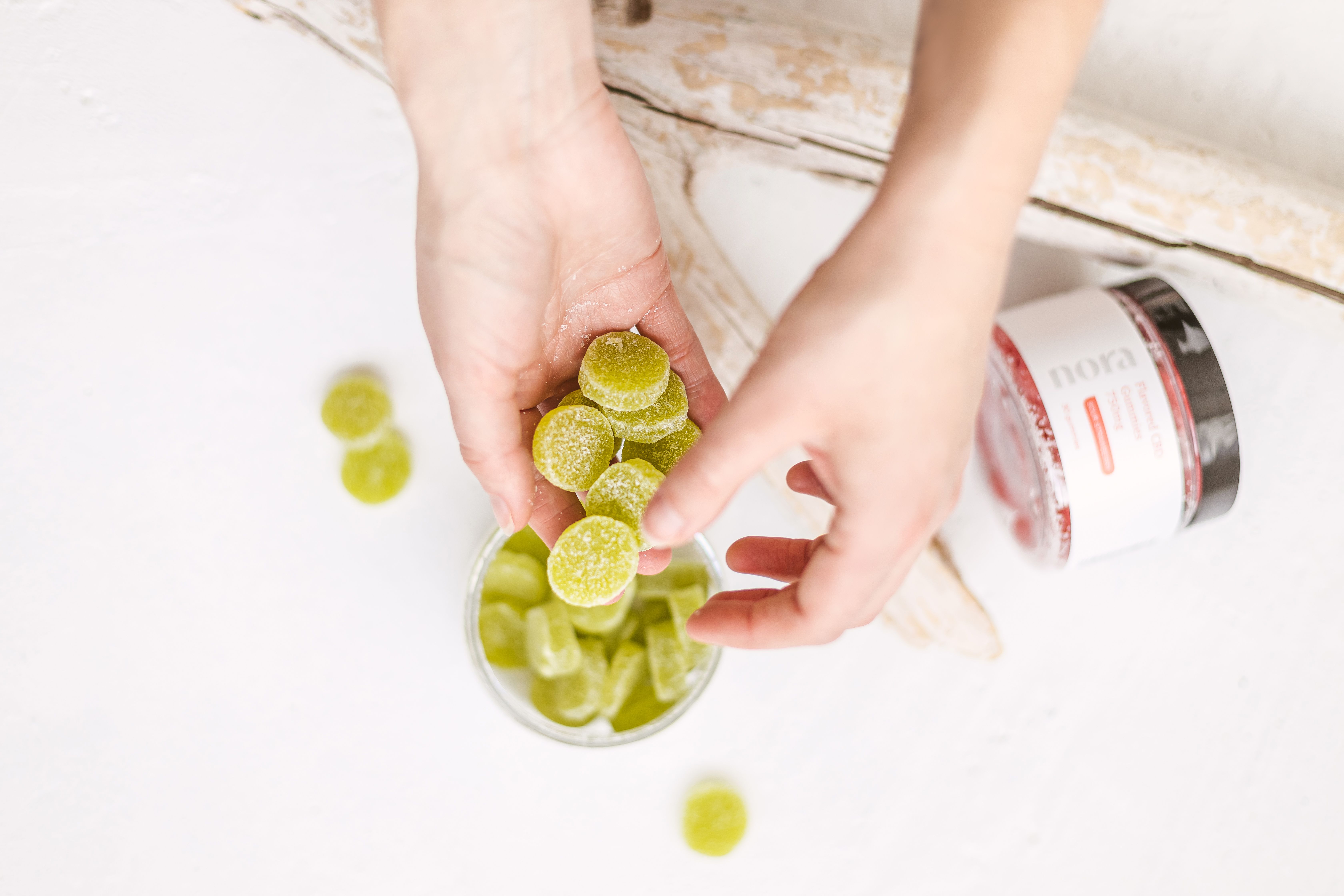 A green jelly supplement in a clear plastic jar is held in on hand with a packaging jar in the background, clean aesthetic background.