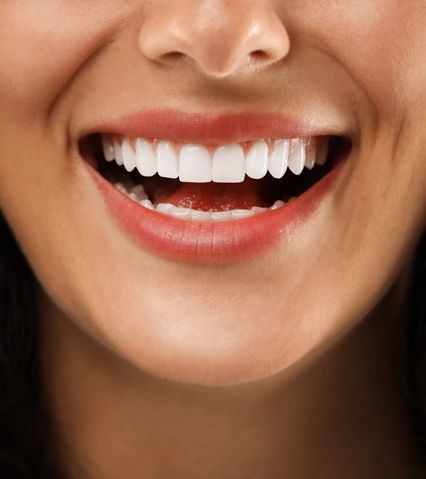 Zâmbet larg cu dinți albi și buze roz pe piele cu ton cald.