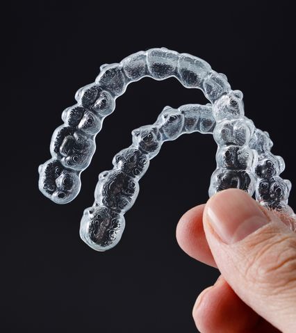 Mână care ține aliniere dentară transparentă pentru dinți pe fundal negru.