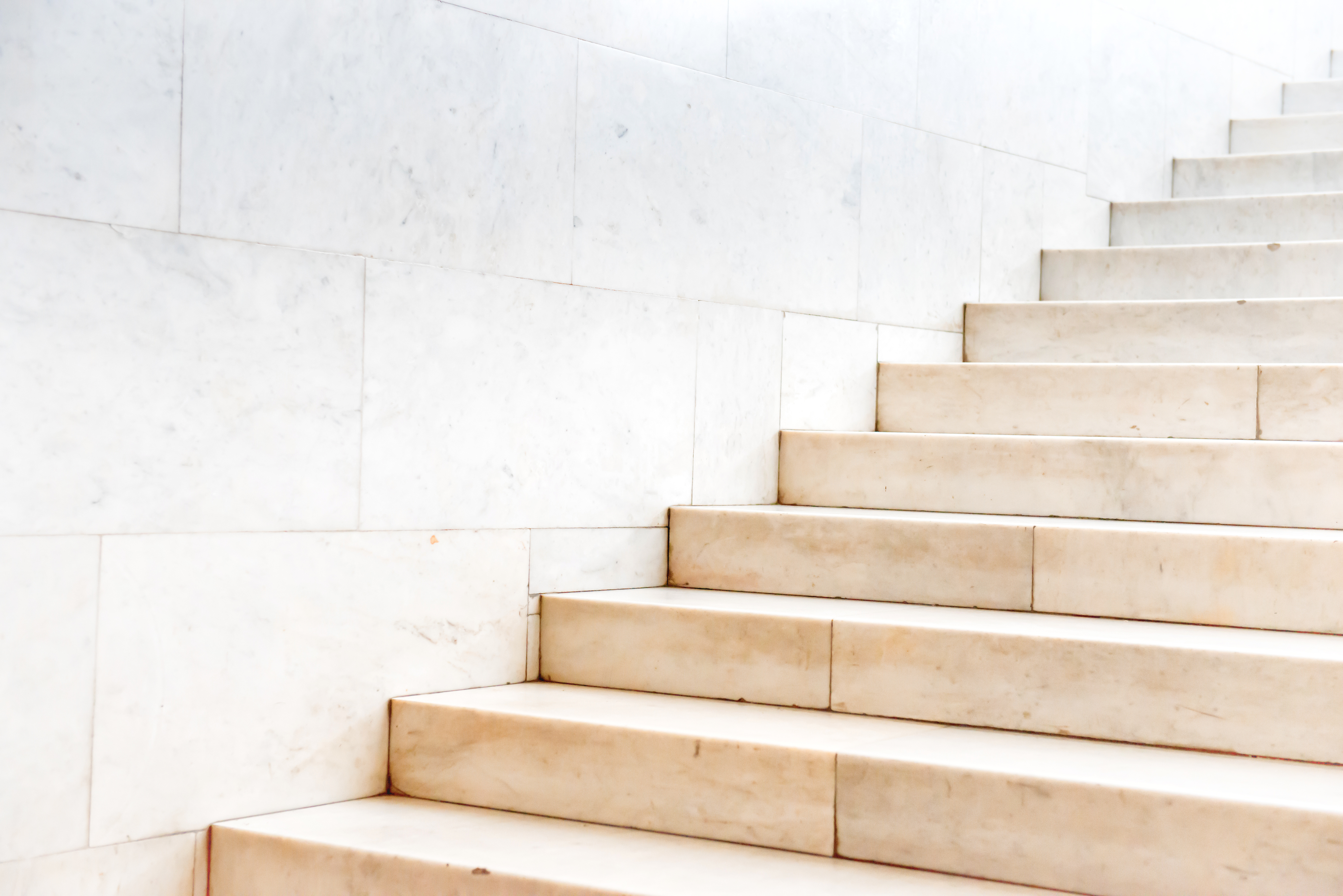 Close-up of beige marble stairs against a white marble tiled wall.